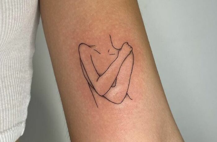 Self-love tattoo of a woman hugging herself on arm.