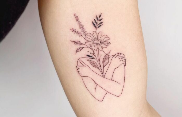 Woman with self-love tattoo featuring arms hugging and flowers.