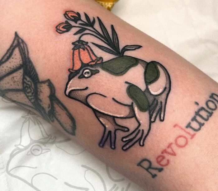 Frog tattoo with "Revolution" text, emphasizing self-love through unique body art.