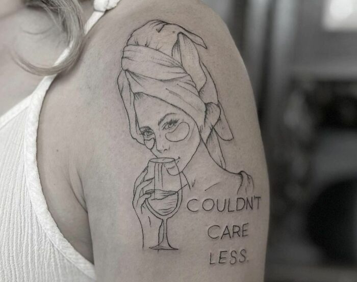 Self-love tattoo of a woman with a glass and text "Couldn't care less" on an upper arm.