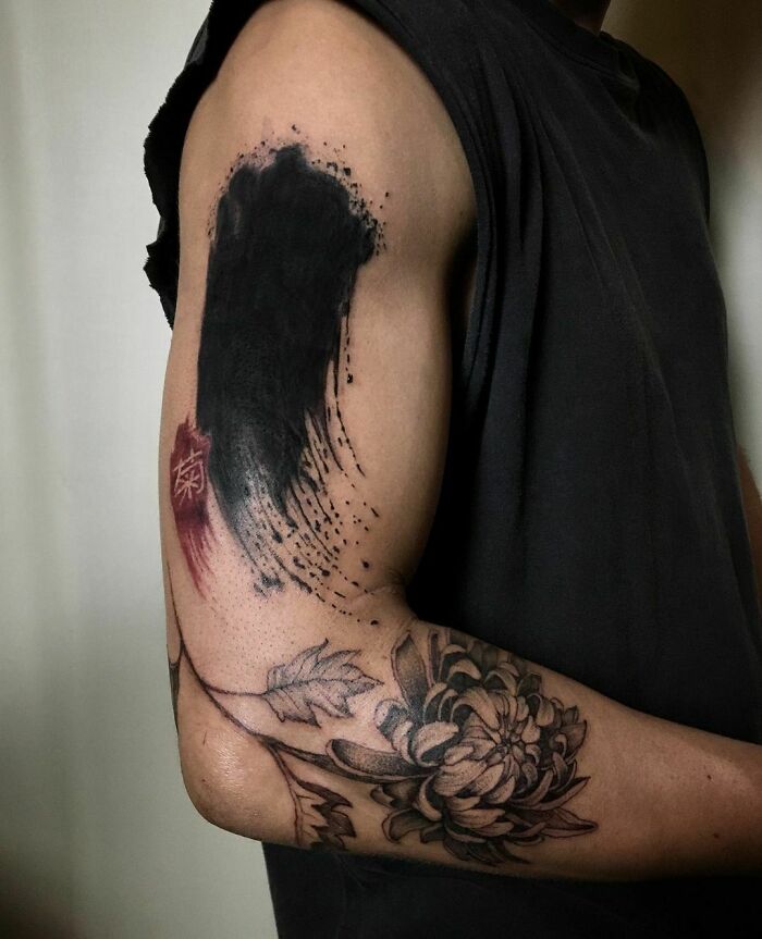 Floral tattoo featuring elegant flower designs on a person's upper arm, with a bold black ink splash above.