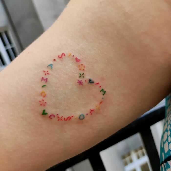 Heart-shaped self-love tattoo with colorful letters and symbols.