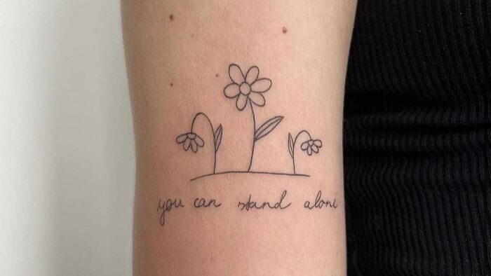 Self-love tattoo of flowers with text "you can stand alone" on an arm, symbolizing empowerment and independence.