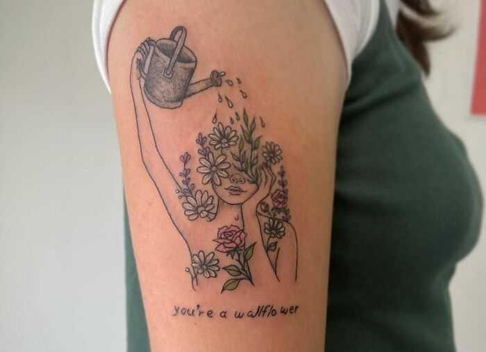 Self-love tattoo: woman watering flowers on head with "You Are A Wallflower" text on arm.