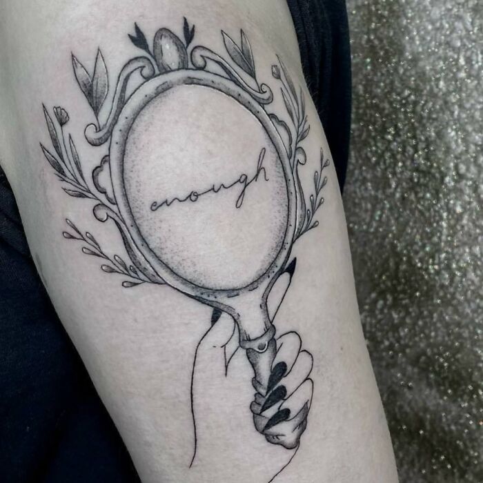 A self-love tattoo of a vintage mirror with "enough" written inside, symbolizing empowerment and self-acceptance.