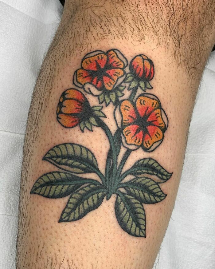 Colorful flower tattoo with red and orange blossoms and green leaves on skin.
