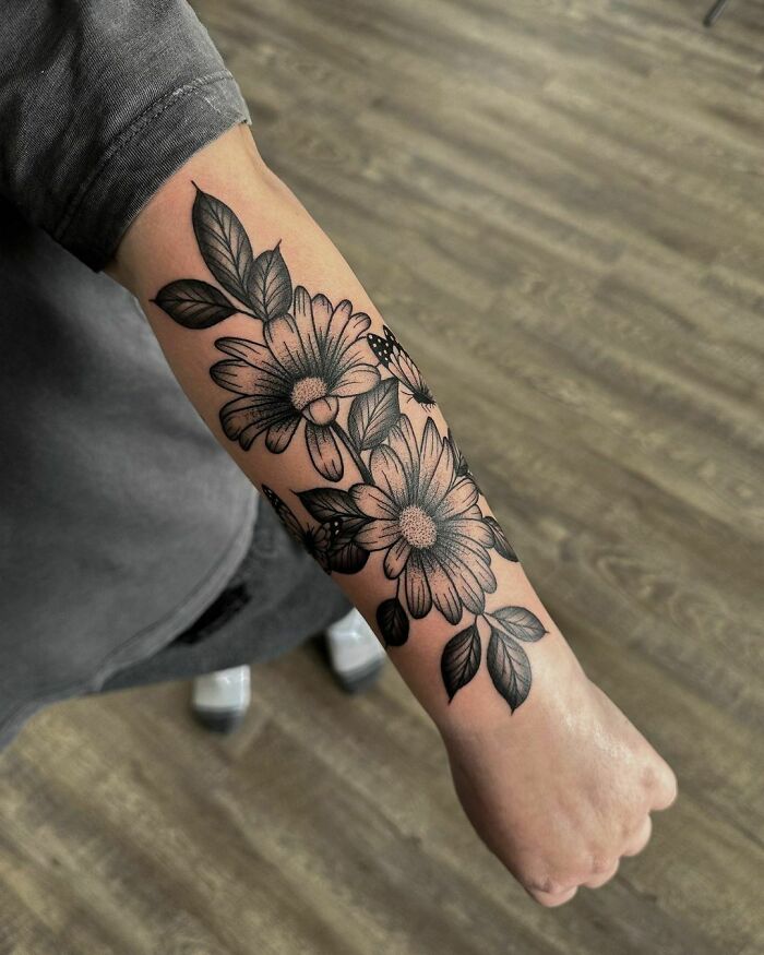 Floral tattoo design with elegant daisies and leaves on a forearm, showcasing beauty and intricate artistry.