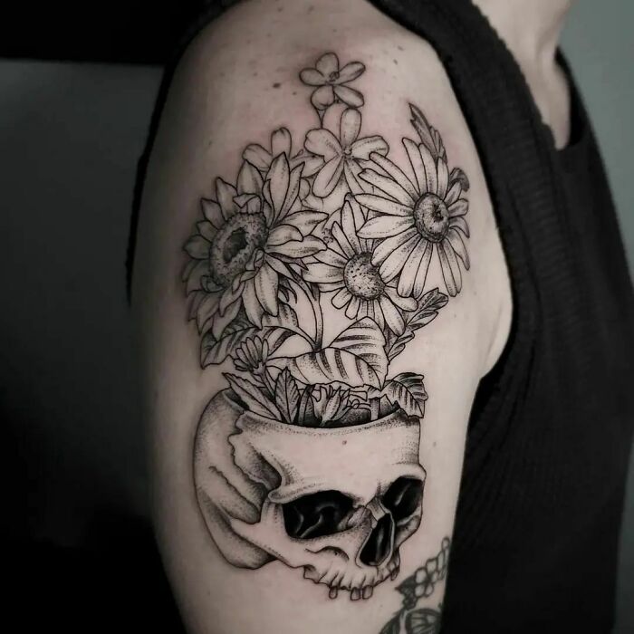 Skull and flower tattoo on upper arm, depicting daisy blooms emerging from a skull design.