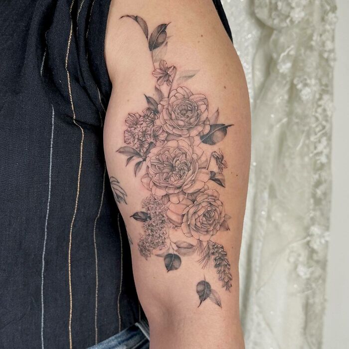 Floral tattoo with detailed roses and leaves on upper arm, creating a blossoming effect on the skin.
