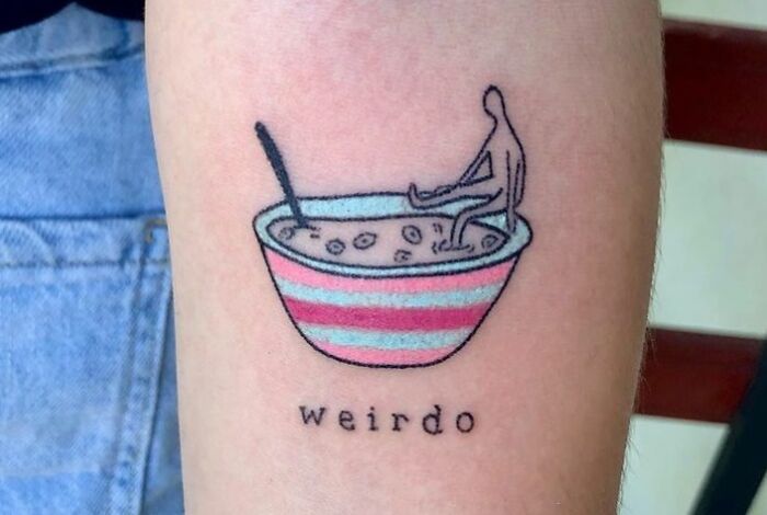 Minimalistic self-love tattoo of a figure in a striped bowl with "weirdo" text below, depicting empowerment and individuality.