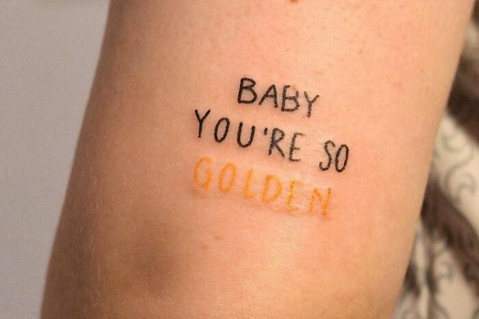 Tattoo reading "Baby You're So Golden" in black and gold, celebrating self-love.