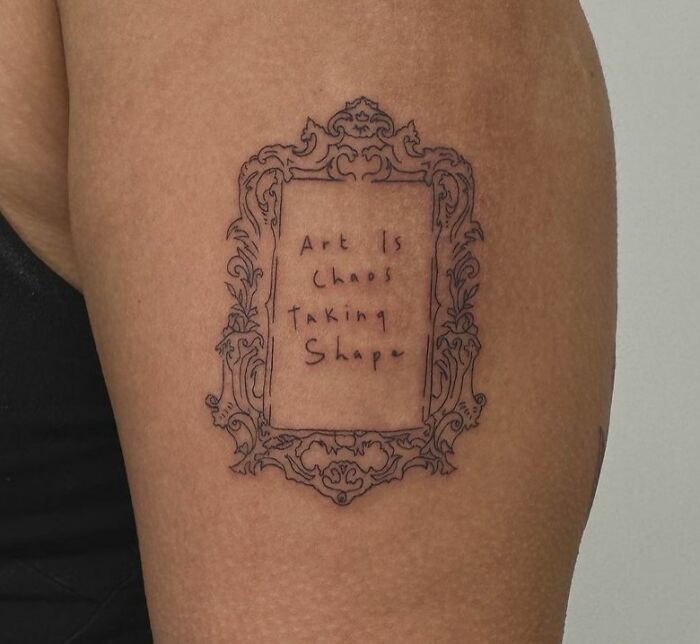 "Artistic self-love tattoo with ornate frame and the phrase 'Art Is Chaos Taking Shape' on a person's arm."