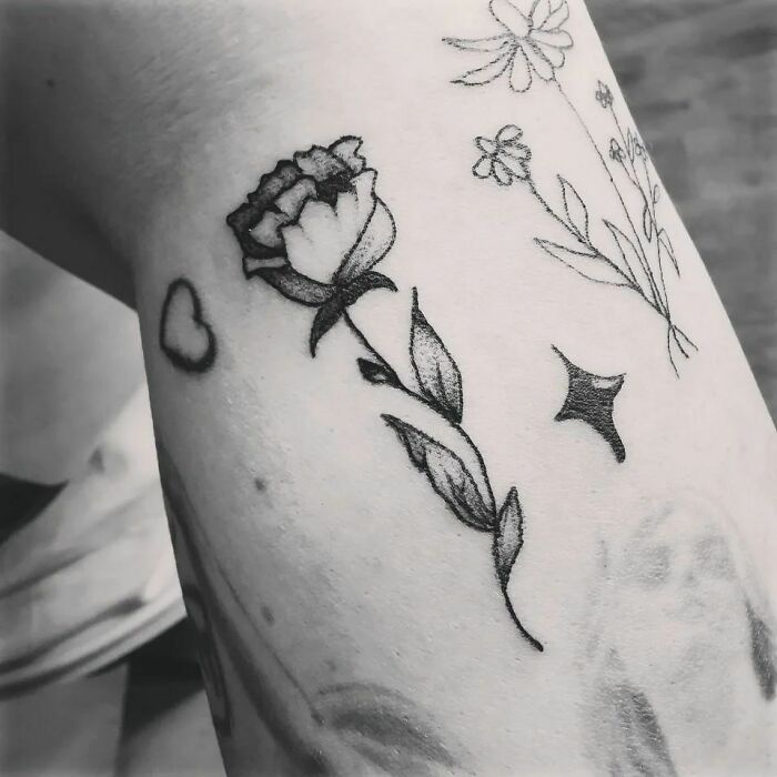 Black ink flower tattoo on arm featuring a rose and wildflowers, creating a blossoming effect on the skin.