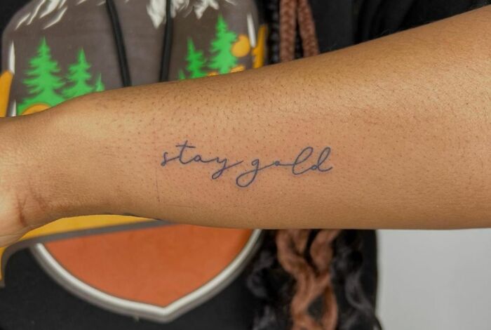 Self-love tattoo with the phrase "Stay Gold" on a forearm, celebrating individuality and personal empowerment.