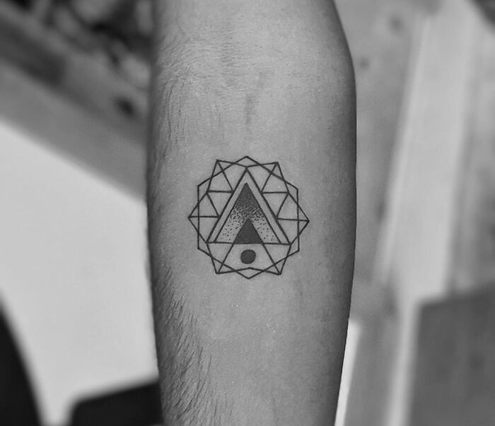 Black geometric tattoo design on forearm featuring patterns of triangles and circles.