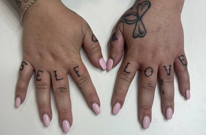 "Self Love" finger tattoos on both hands with pink nail polish.