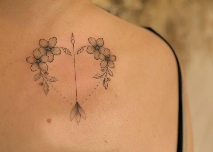 Self-love tattoo featuring flowers and an arrow, symbolizing personal growth on the back.