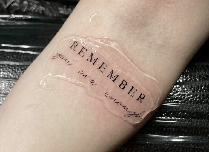 Self-love tattoo with the phrase "Remember, You Are Enough" on skin, celebrating self-worth and individuality.