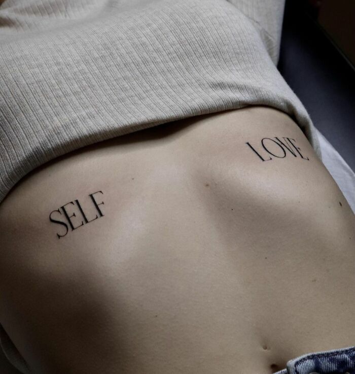 Ribcage tattoo with "Self Love" text, celebrating self-love.