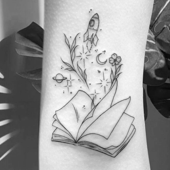 Self-love tattoo with an open book, rocket, planets, and floral designs symbolizing growth and inspiration.