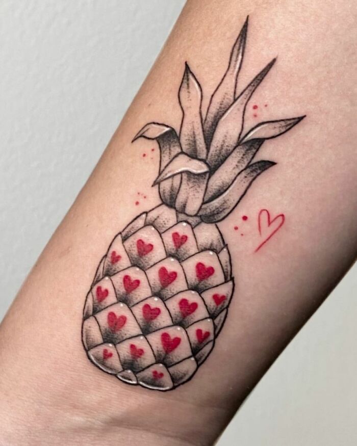 Pineapple tattoo with red hearts symbolizes self-love on an arm.