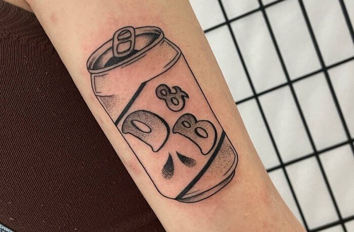 Tattoo of a soda can on an arm, symbolizing self-love with bold black outlines and shading.