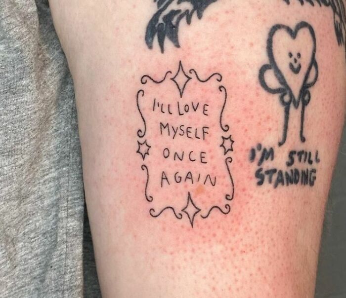 Self-love tattoos with quotes "I'll love myself once again" and "I'm still standing" on arm.