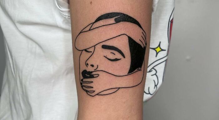 Tattoo of a face with arms wrapped around for self-love on an upper arm, expressing deep meaning and empowerment.