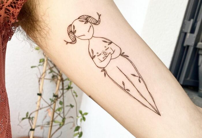 Minimalist self-love tattoo featuring a horned figure with delicate floral accents on the arm.