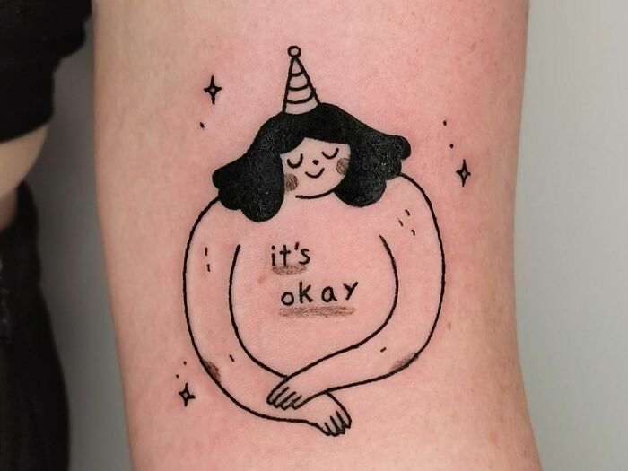 Self-love tattoo featuring a figure with a party hat and the words "it's okay."