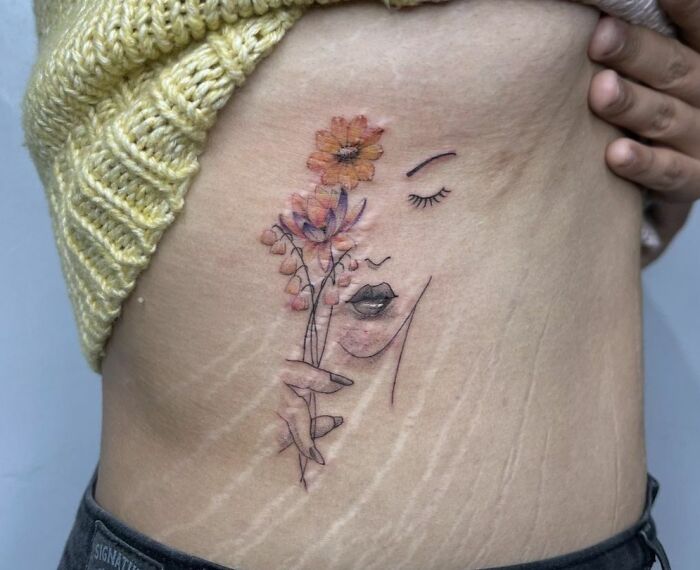Floral self-love tattoo on side, featuring a serene face outline with orange flowers against natural skin texture.