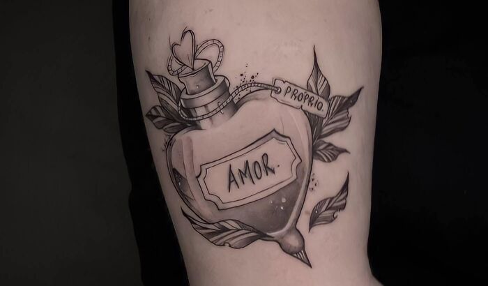 Self-love tattoo with a heart-shaped bottle labeled "Amor Proprio," surrounded by leaves.