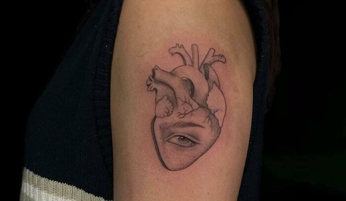 Self-love tattoo of an anatomical heart with an eye design on an arm.