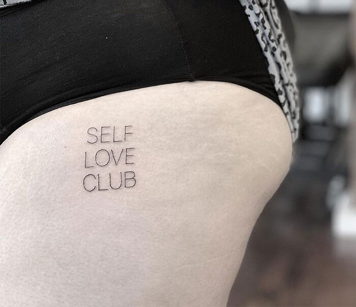 "Self-love tattoo reading 'Self Love Club' on upper thigh, promoting empowerment and self-acceptance."