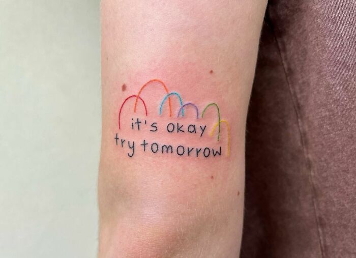 Self-love tattoo with rainbow arches and the words "it's okay try tomorrow" on an arm for inspiration and empowerment.