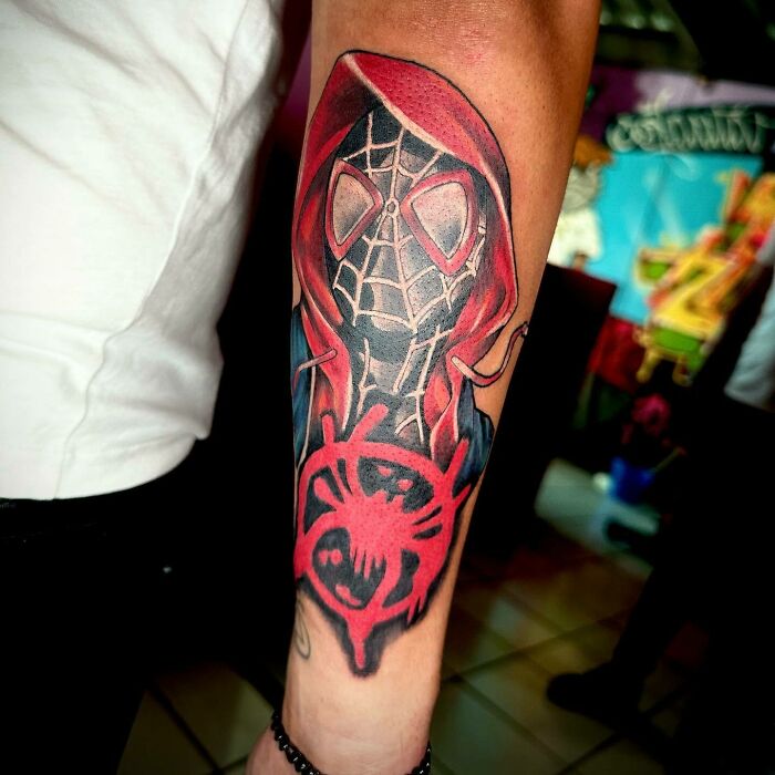 Marvel tattoo of Spider-Man on a forearm, featuring red and black design with web pattern and mask.