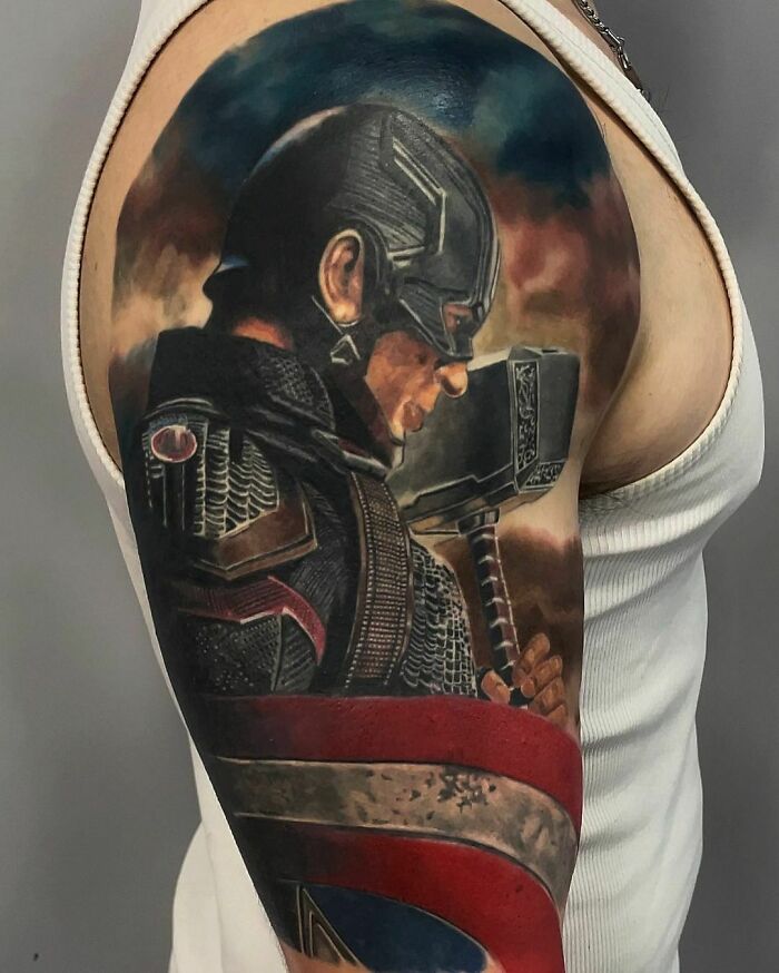 Marvel tattoo of a superhero on an arm, featuring a shield and hammer, showcasing intricate design and vivid colors.
