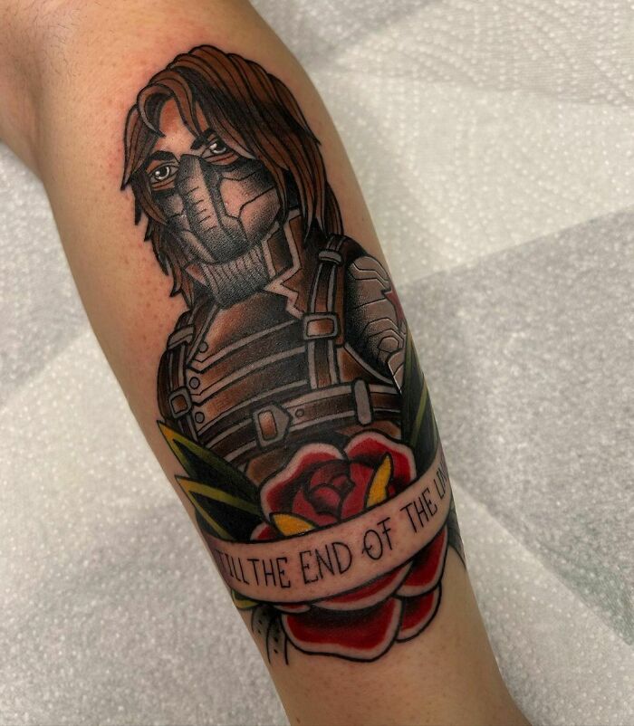 Marvel tattoo featuring a masked Winter Soldier character above a colorful rose with text, showcasing superhero-inspired body art.