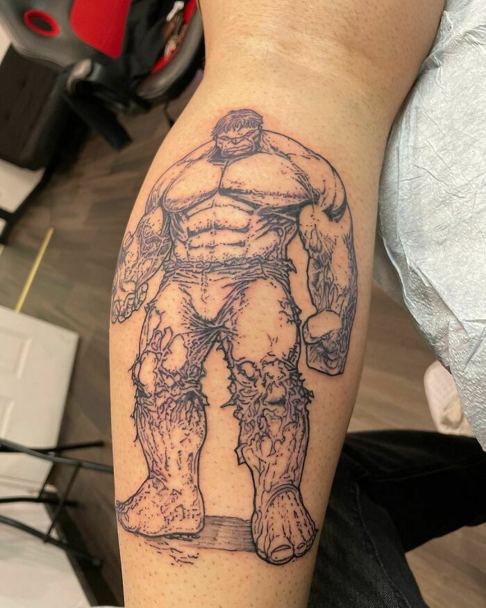 Marvel tattoo of a muscular superhero in black ink on a person's leg.