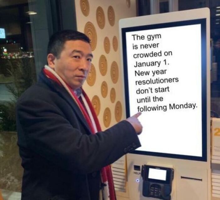 Man pointing at a sign with a funny gym meme about New Year resolutions and gym crowding.