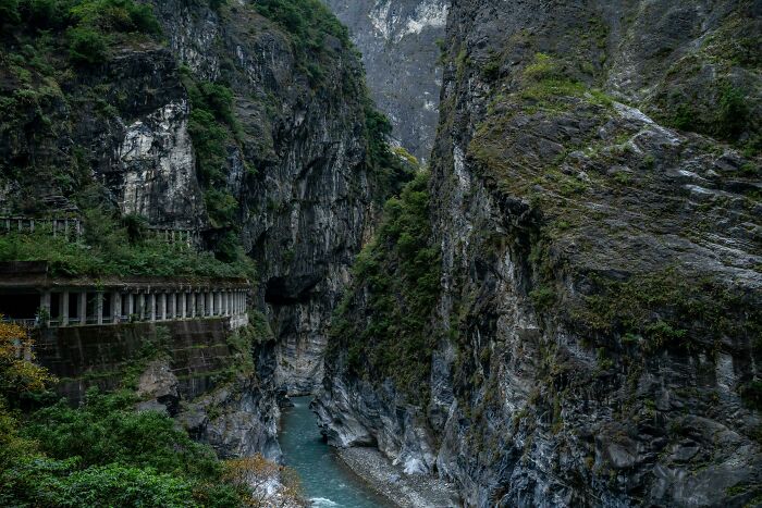Tunnel carved into steep rocky cliffs over a river, showcasing the beauty of well-planned infrastructure in a rugged natural landscape.