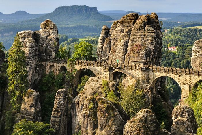 Stone bridge connecting rocky cliffs surrounded by lush greenery, showcasing the beauty of well-planned infrastructure.
