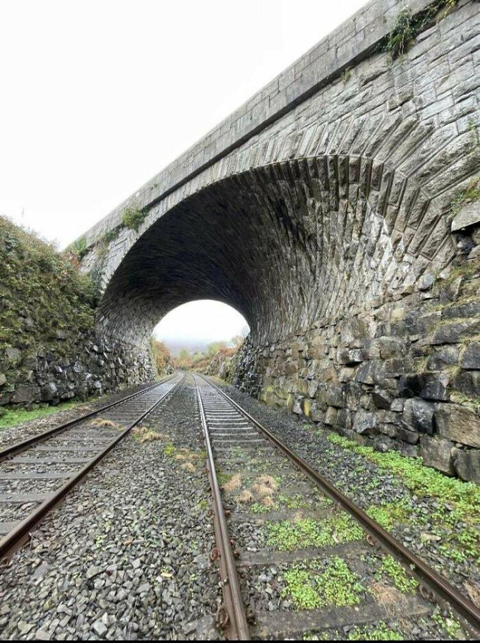 Stone arch bridge over railway tracks showcasing the beauty of well-planned infrastructure in a natural setting.