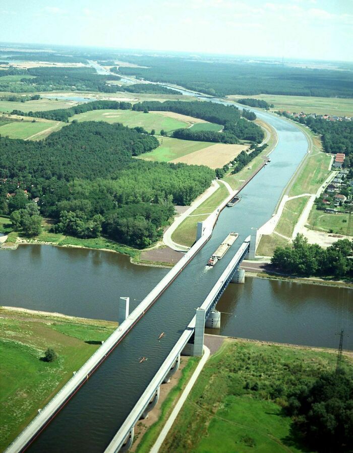 Aerial view of a well-planned infrastructure showing a canal bridge over a river with surrounding green fields and forest.