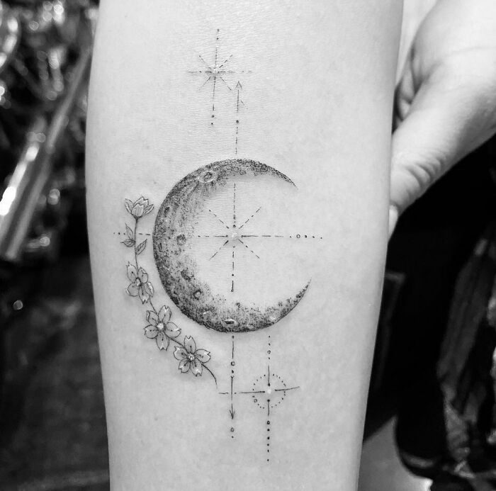 Celebrity tattoo of a half-moon design with flowers and dotted stars on forearm.