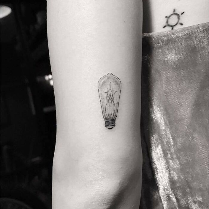 Light bulb tattoo on forearm, celebrity-inspired ink design.