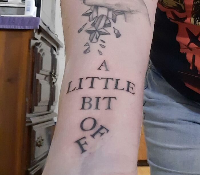 Word tattoo on forearm with geometric design above, featuring the phrase "A LITTLE BIT OF."