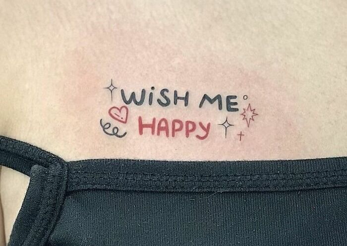 Word tattoo on skin reading "Wish Me Happy" with decorative elements.