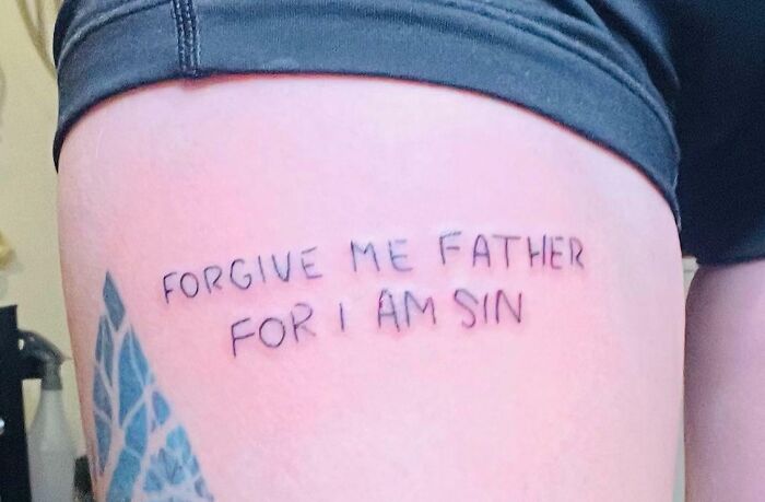 Word tattoo on thigh says "Forgive me father for I am sin" in black ink.