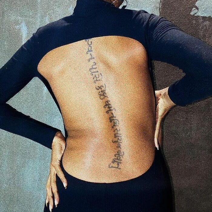 Back with a vertical script-inspired word tattoo, wearing a black open-back top.